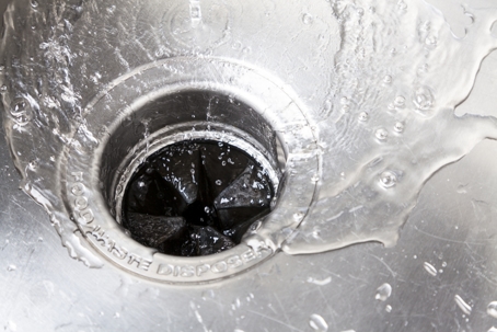 A close-up view of water flowing into a garbage disposal in a stainless steel sink. | Blazer Heating, Air, and Plumbing
