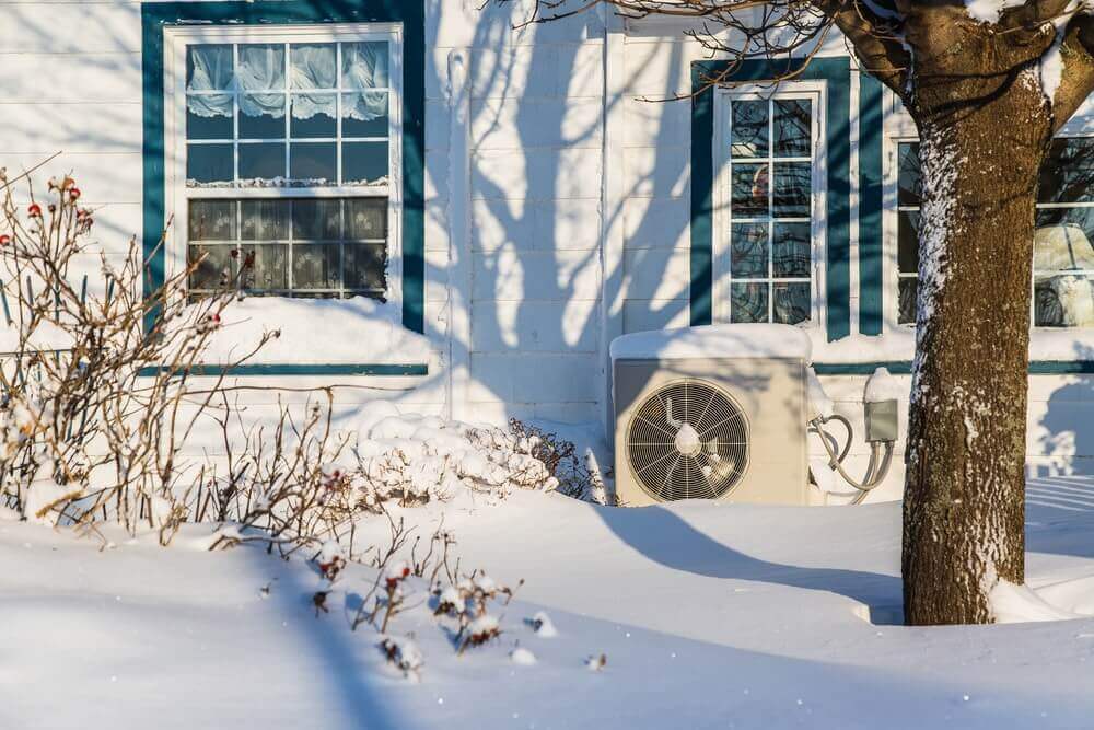 A snow covered home, yard, and heat pump.