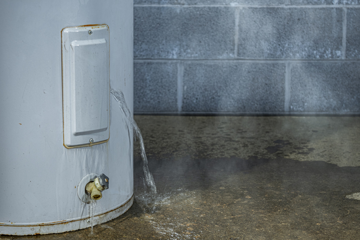 A close-up of a water heater leaking on a basement floor. | Blazer Heating, Air, and Plumbing